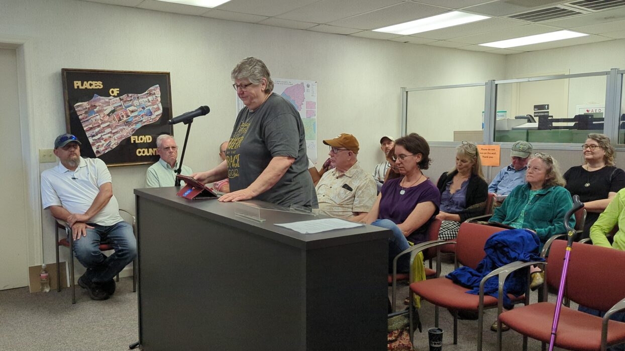 Floyd member LA (she/they), a tall dyke with grey hair giving remarks at a podium during Floyd, VA Board of Supervisors Meeting. 